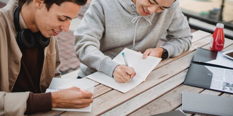 Man in Gray Hoodie Writing on White Paper