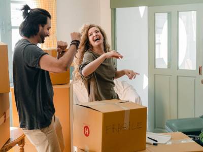 Cheerful laughing couple in casual clothes having fun and dancing together while unpacking carton boxes after moving into new contemporary apartment