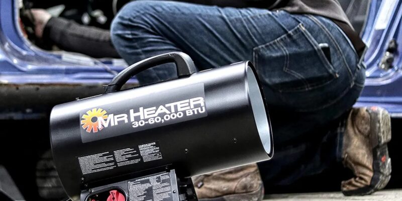 A man using an air heater to warm up a car