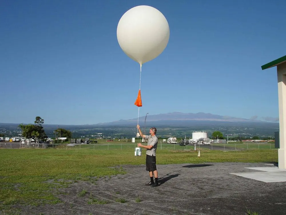 A man joyfully holds a large white balloon high in the air