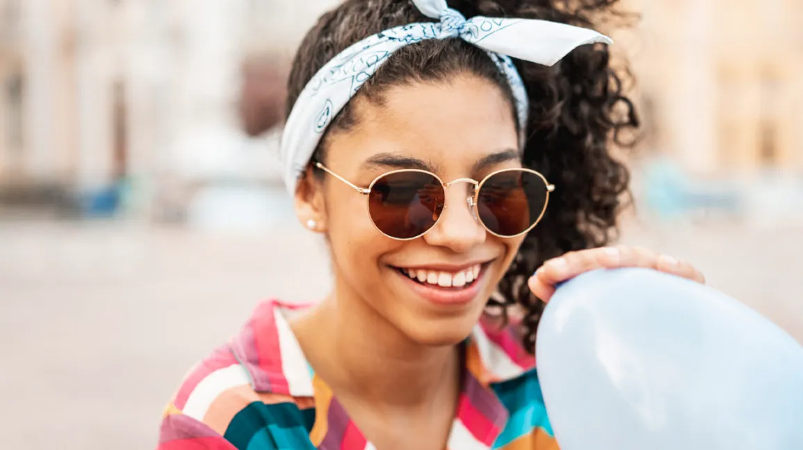 A woman with sunglasses and a headband holds a balloon