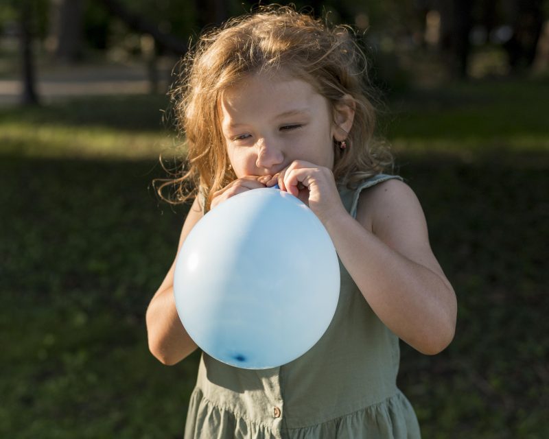 A small girl blowing air into a balloon